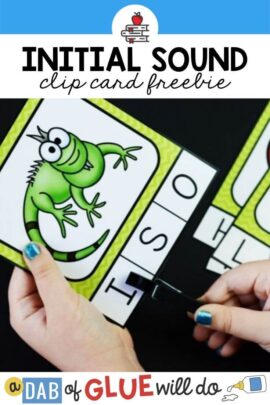 Child's hands holding a card with an iguana on it with the letters "I," "S," and "O" on the bottom. The child is using a black clothespin to clip the letter I.